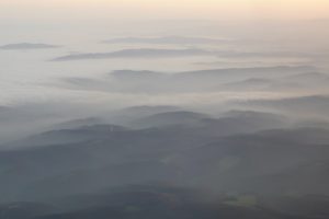 Blick aus Flugzeug auf Wolken, Bergkuppen, Wald