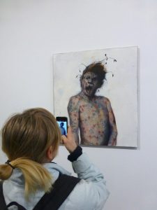 Eine junge Frau fotografiert ein Gemälde: Mann mit aufgerissenem Mund und nacktem Oberkörper.