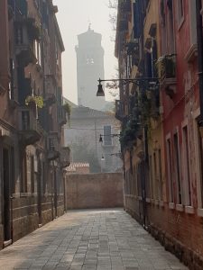 Eine leere Gasse in Venedig, im Hintergrund ein Turm noch im Nebel