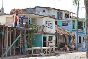 Drei Arbeiter auf dem Dach eines eingeschossigen eingerüsteten Hauses (mit alten Säulen) bei der Arbeit, rechts daneben weitere Häuser (Baracoa, Cuba)