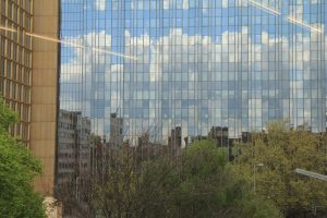 In einem Berliner Hochhaus spiegeln sich Baumkronen, Hochhäuser und Wolken.