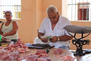Ein Fleischer zählt sein Geld, links eine Frau, rechts eine Waage, im VG Fleisch. (Markthalle Camagüey
